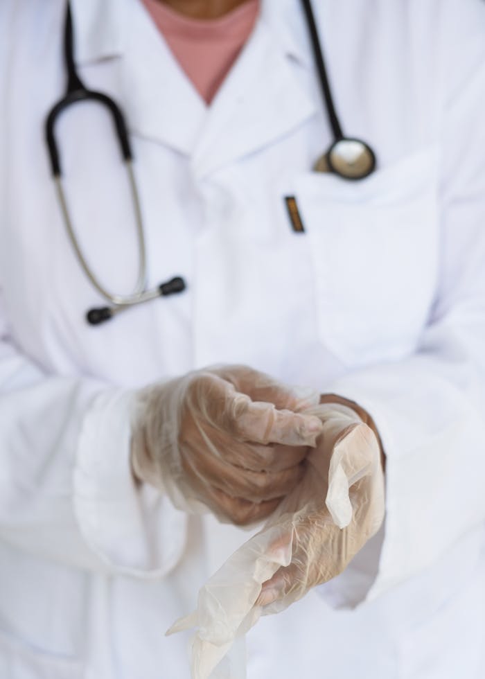 services-01 Faceless ethnic medical worker in lab coat and stethoscope taking of transparent gloves after approaching patients for examination in modern hospital
