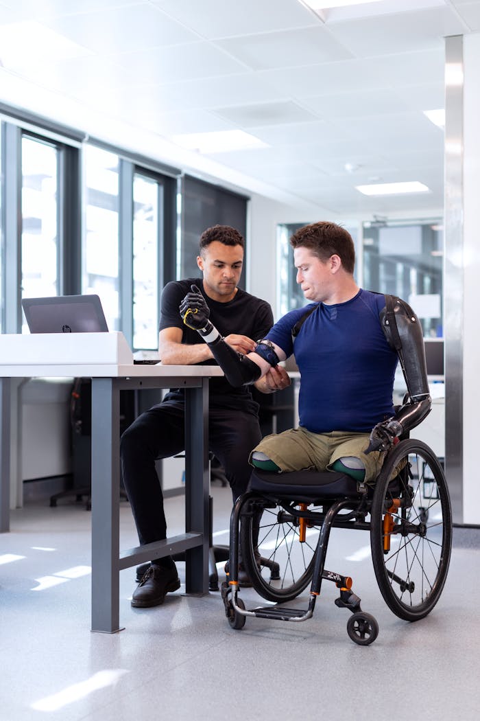 services-03 Engineer adjusts prosthetic arm for seated man in wheelchair, focusing on modern technology in healthcare.