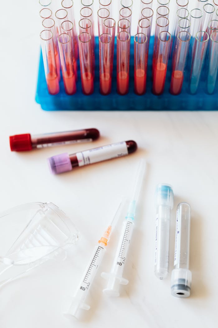 about-us From above of transparent test tubes with colorful liquids placed on blue stand and table near syringes and plastic eyeglasses