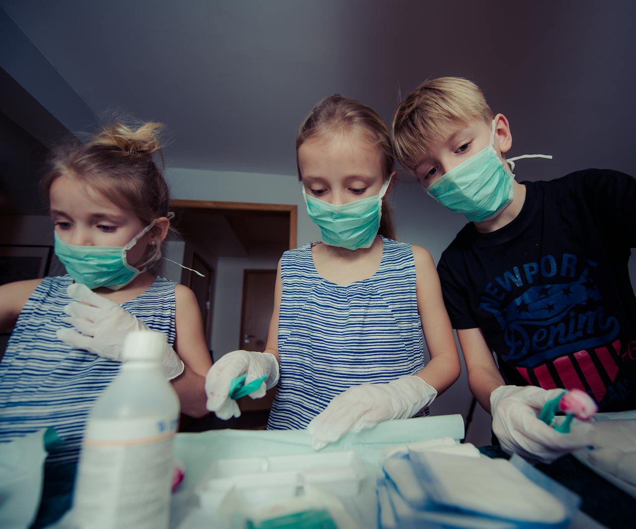 Children pretending to be doctors in a playful indoor setting, wearing masks and gloves.